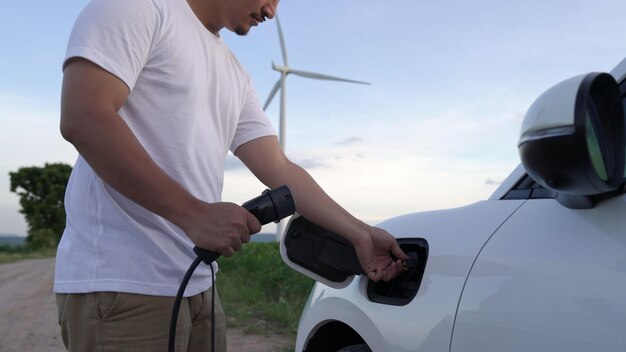 Fortschrittlicher Mann mit seinem Elektroauto Elektrofahrzeug lädt Energie von der Ladestation ...